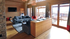 Un interior moderno con techo de madera, pared de piedra, sofá gris, mesa de comedor de madera y un ventanal grande.