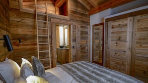 Un dormitorio de cabaña de madera con cama, escalera, baño con lavamanos y un espejo grande.