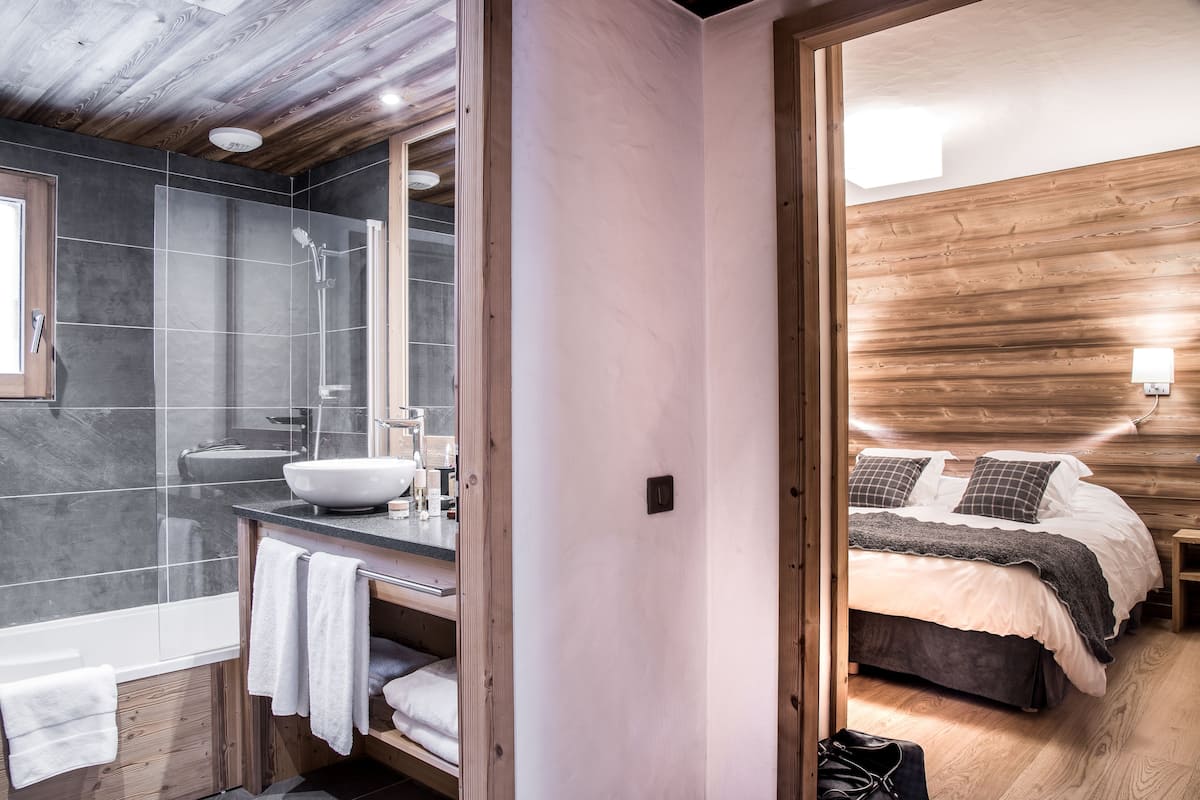 A modern bathroom with a large mirror, a sink, and a shower. The room has wooden walls and a wooden ceiling.