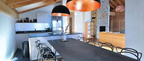 A modern kitchen with a central island, black bar stools, and pendant lighting.