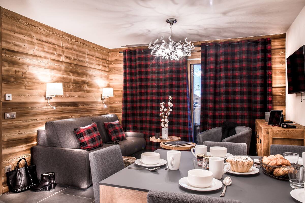 A modern living room with a sofa, a dining table set with plates, cups, and a basket of bread.