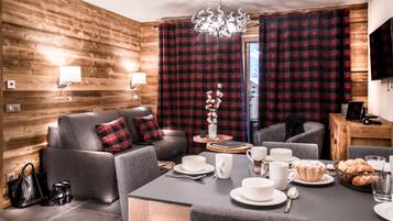 A modern living room with a sofa, a dining table set with plates, cups, and a basket of bread.