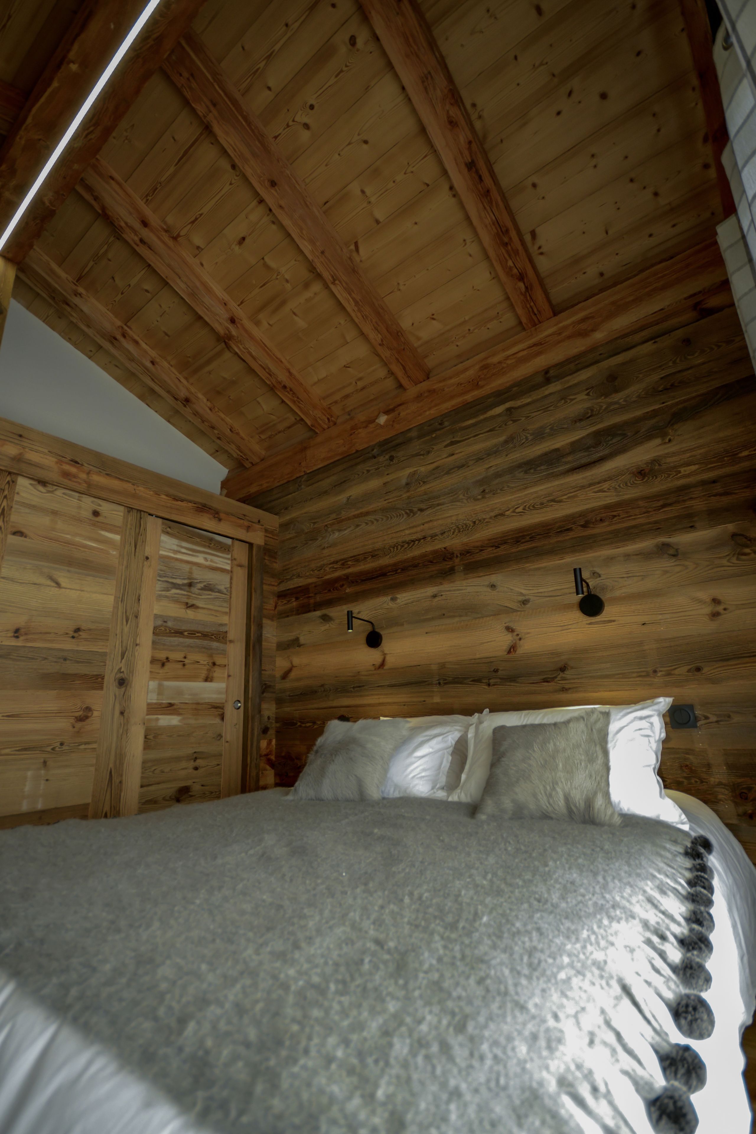 Une pièce de style cabane en bois, avec un lit, un plafond en bois et une porte.