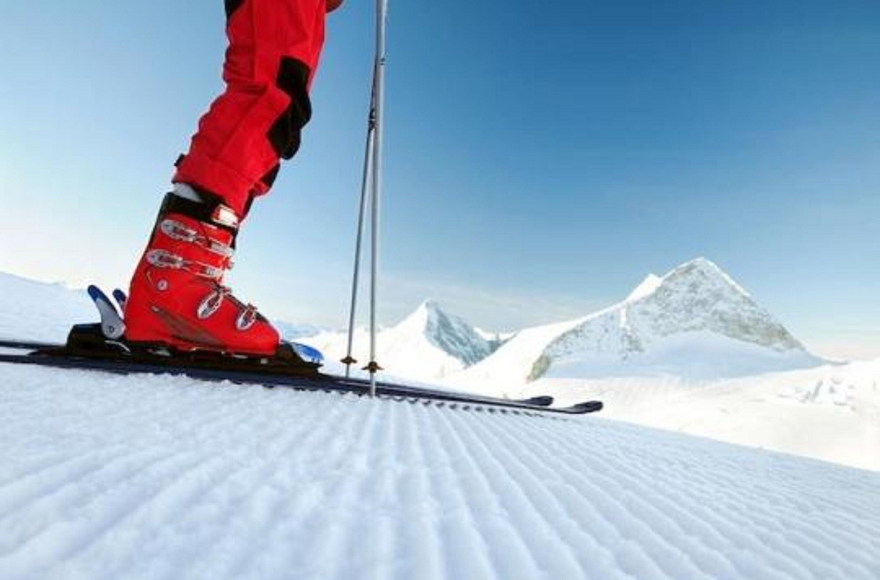 Eine Person fährt auf einem verschneiten Hang mit blauem Himmel und einem Berg im Hintergrund Ski.