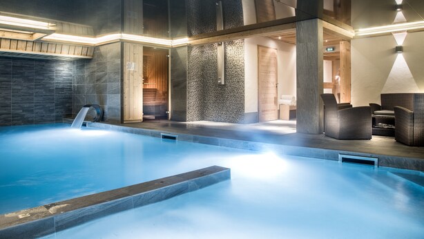 Un área de piscina interior moderna con agua cristalina, detalles de madera y asientos cómodos.