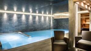 Una piscina interior moderna con suelo azul, rodeada de paredes de piedra y vigas de madera.