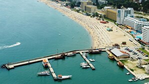 A coastal cityscape with a long beach, a marina with boats, and high-rise buildings. - Hotel Milano (Burgas)