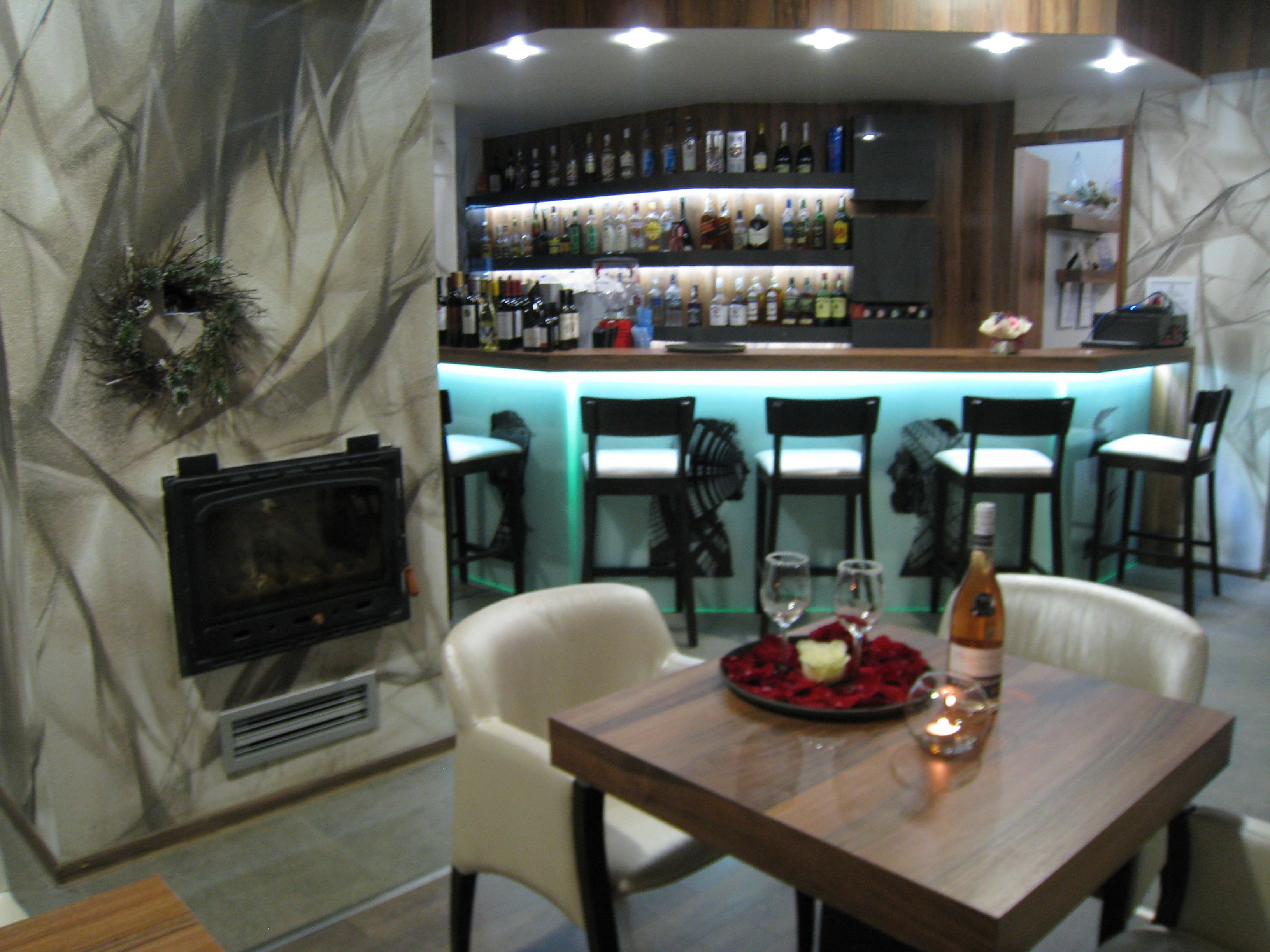 Een bar met een open haard, barstoelen en verschillende flessen drank.