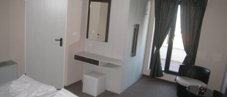 A hotel room with a bed, a small desk, a mirror, a chair, and a window with curtains.