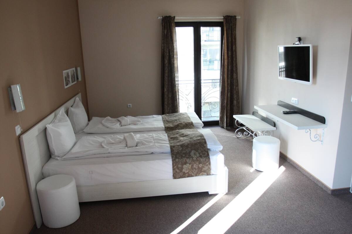 A hotel room with two beds, a bathroom, a TV, and a balcony with curtains.