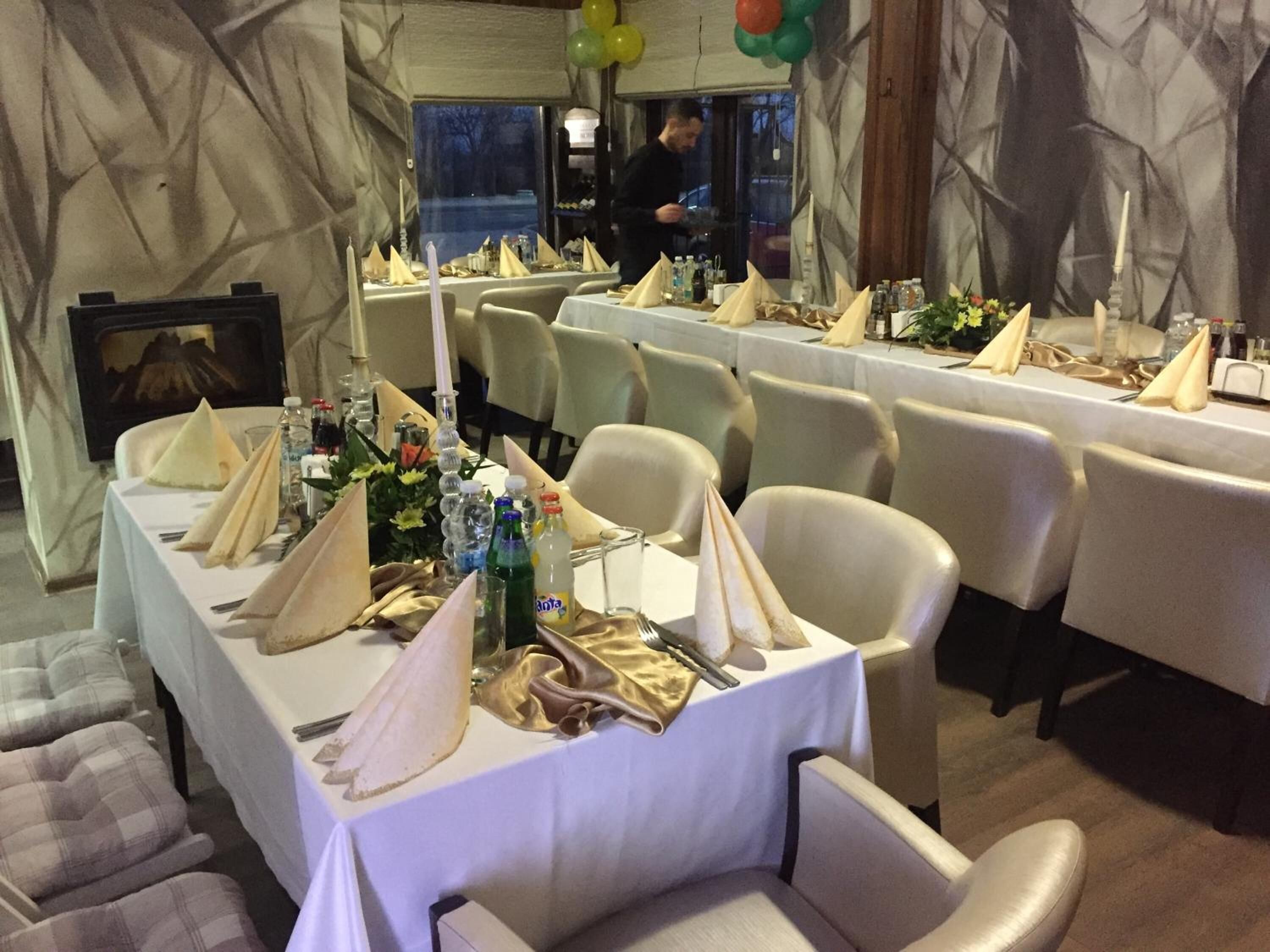 Un salón de banquetes con varias mesas dispuestas para un evento formal, con manteles blancos, servilletas ordenadas y cristalería.