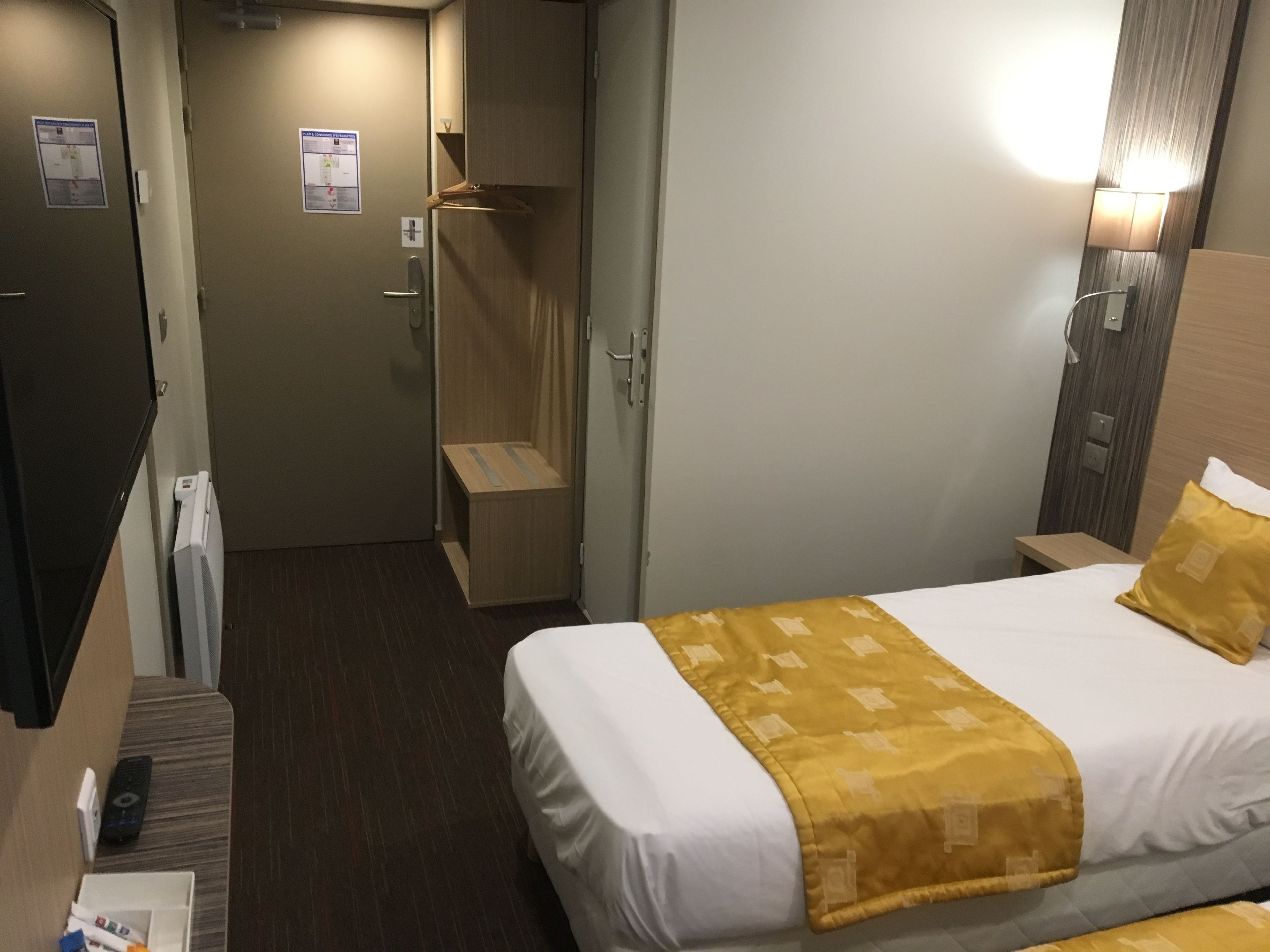 Habitación de hotel con cama, mesita de noche, lámpara y zona de ducha.