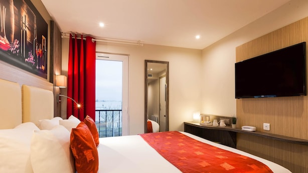 Une chambre d’hôtel avec un lit, une télévision, un miroir et un balcon avec des rideaux rouges.
