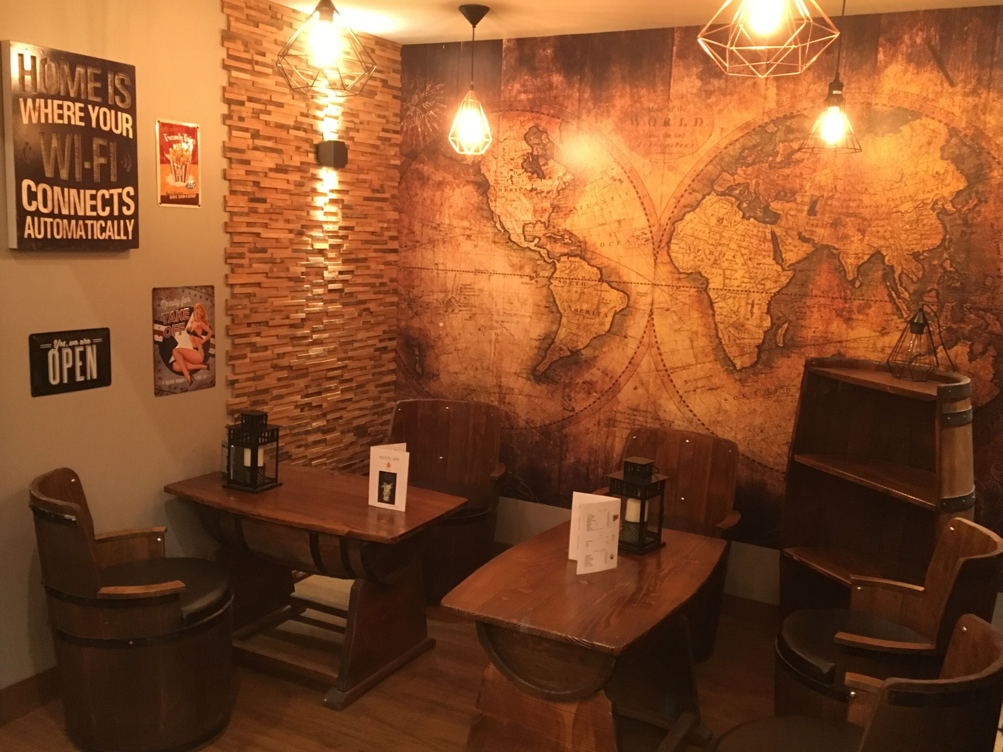 A cozy restaurant with wooden tables and chairs, a world map mural, and a sign stating "Home is where your Wi-Fi connects automatically."