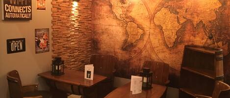 A cozy restaurant with wooden tables and chairs, a world map mural, and a sign stating "Home is where your Wi-Fi connects automatically."