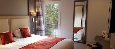 Une chambre d’hôtel avec un grand lit, un miroir, un balcon avec vue et une petite table avec une bouilloire.