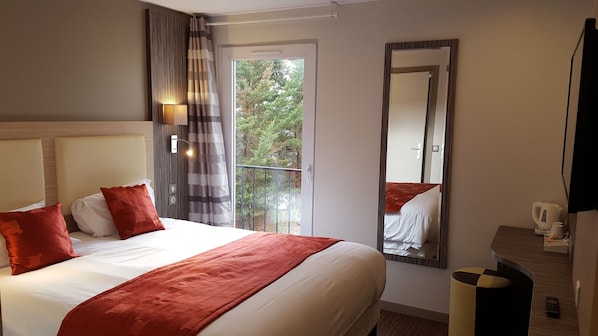 Une chambre d’hôtel avec un grand lit, un miroir, un balcon avec vue et une petite table avec une bouilloire.