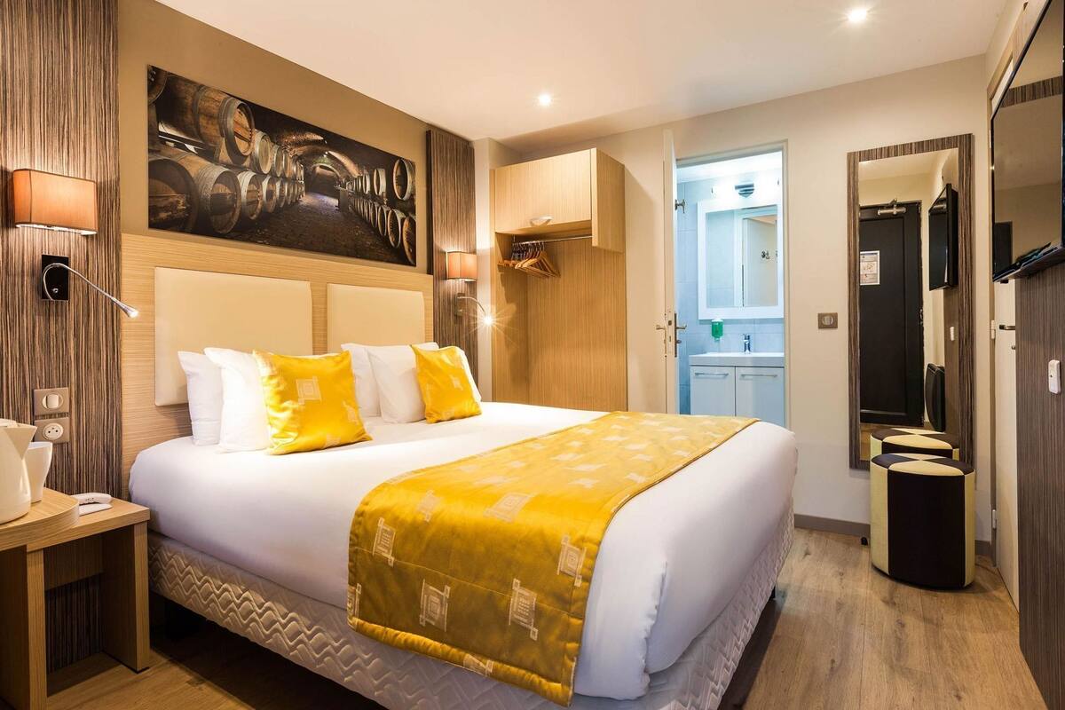 Habitación de hotel con una cama grande, un cuadro de barriles de vino, cabecero de madera, mesita de noche con lámpara y un espejo.