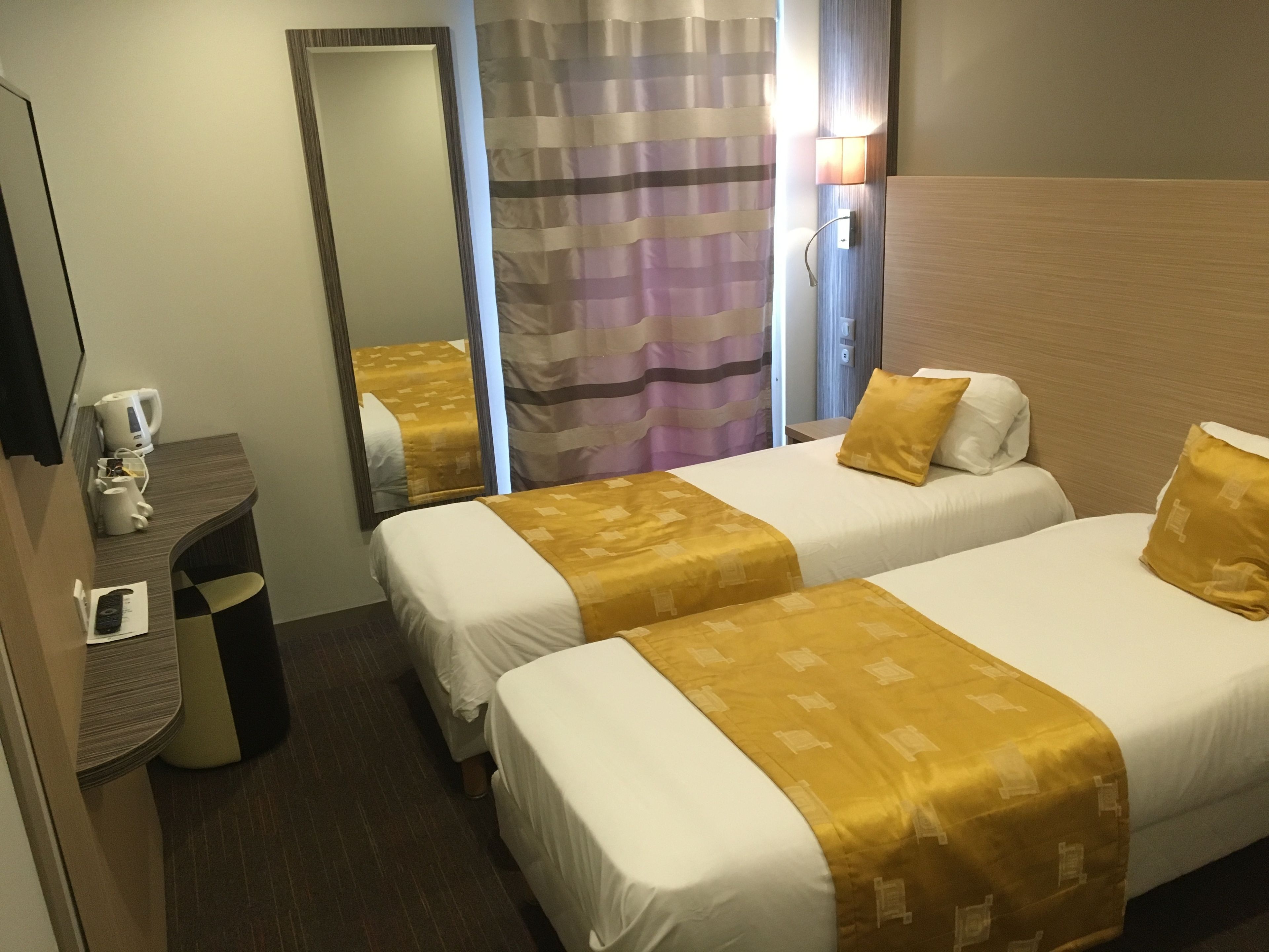 Une chambre d’hôtel avec deux lits, un bureau avec une machine à café, un miroir et un rideau.