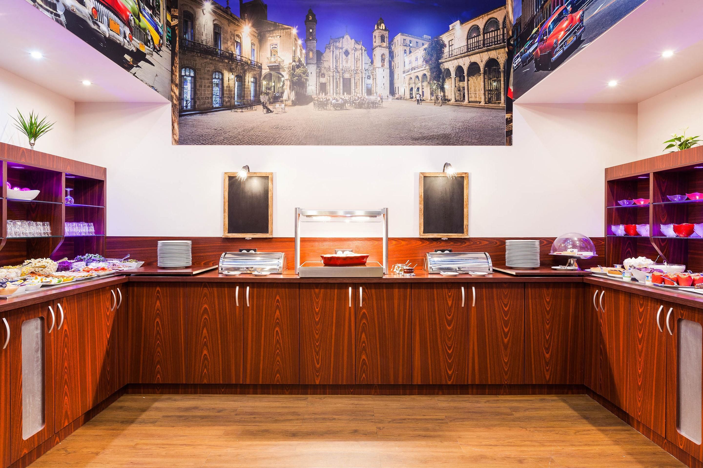 A buffet area with wooden cabinets, a central serving station, and a large cityscape mural on the wall.