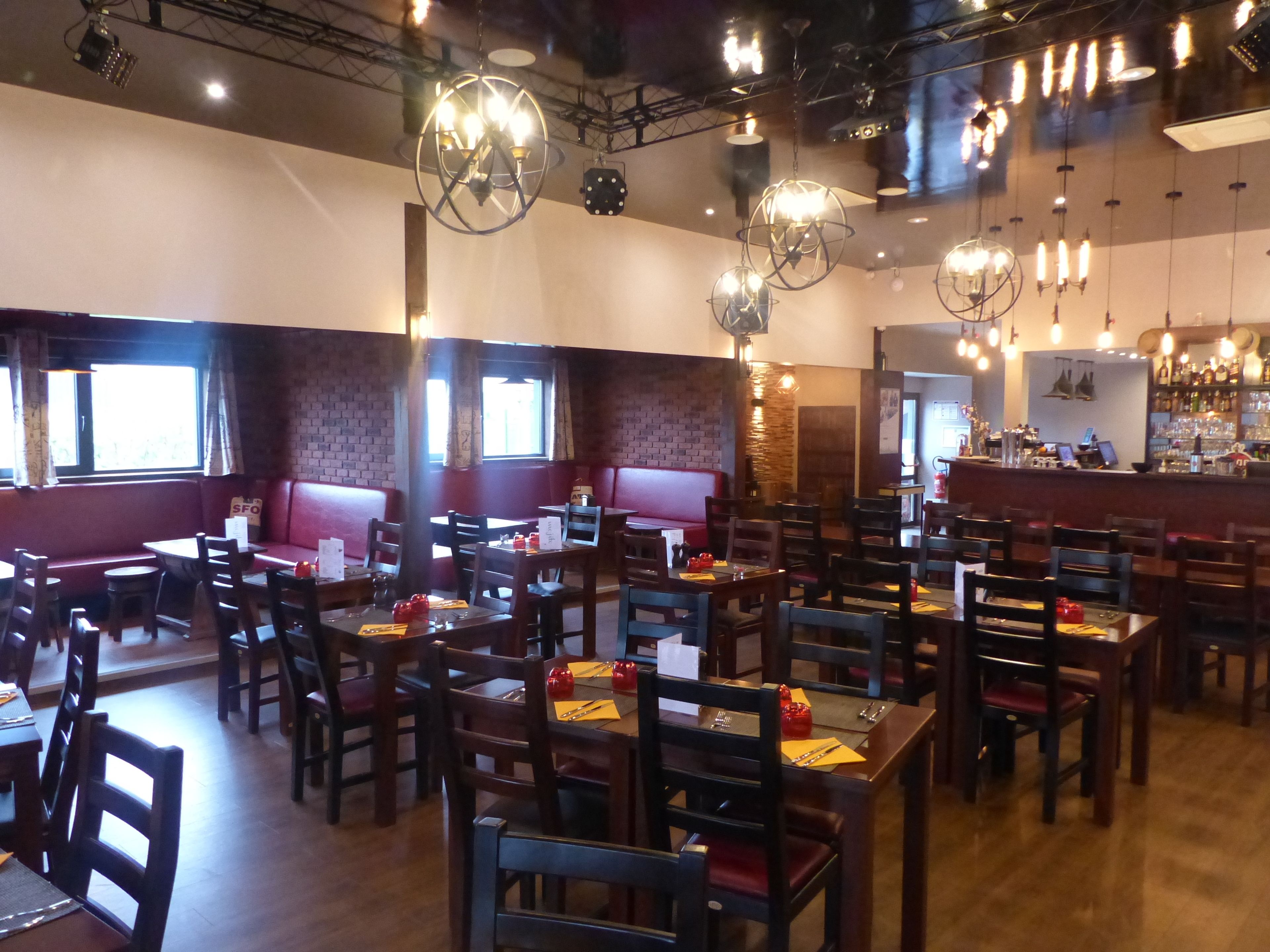 Ein Restaurant mit Sitzboxen und Tischen, Holzstühlen und hängenden, kugelförmigen Leuchten.