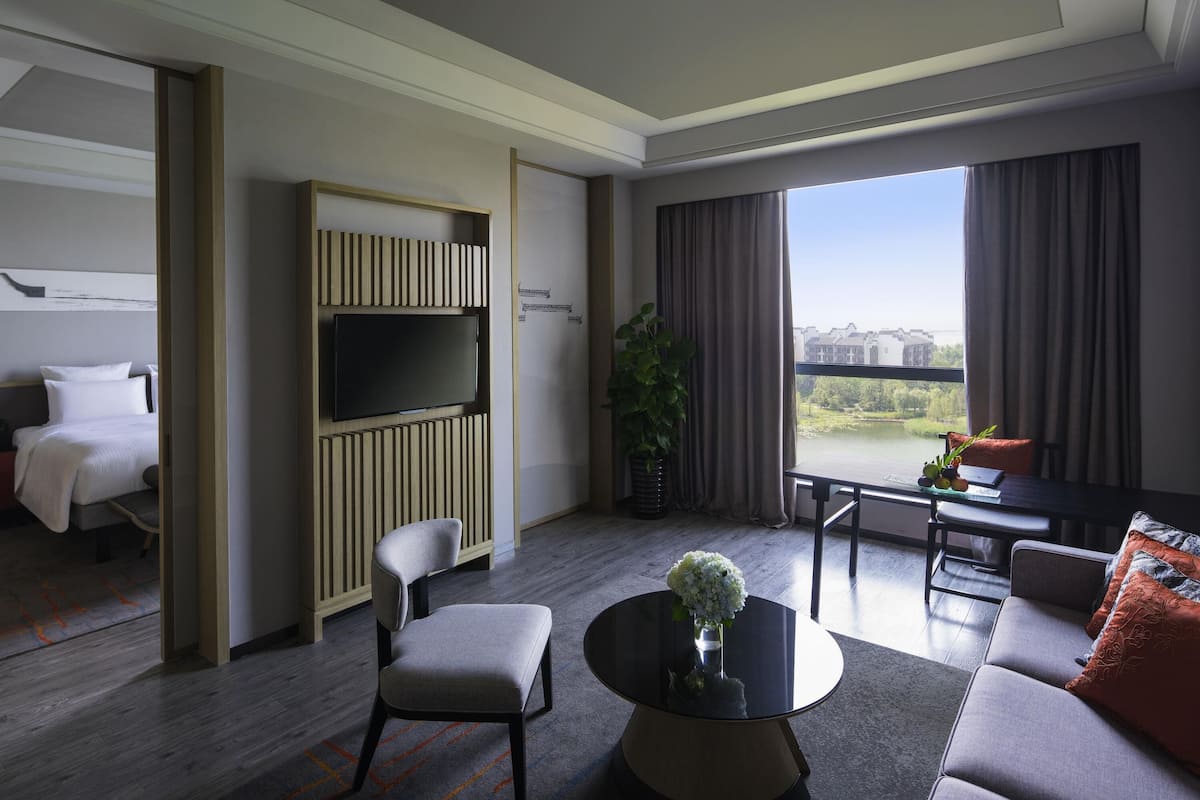 A hotel room with a bed, a TV, a sofa, a dining table, and a view of a body of water.