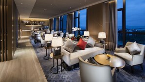 A modern hotel lobby with a long reception desk, seating area with sofas and armchairs, and large windows offering a view of the cityscape. - Pullman Hefei Sunac (Hefei)