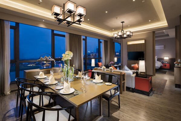 A modern hotel dining area with a large table set for a meal, a city view, and a cozy seating area with a TV. - Pullman Hefei Sunac (Hefei)