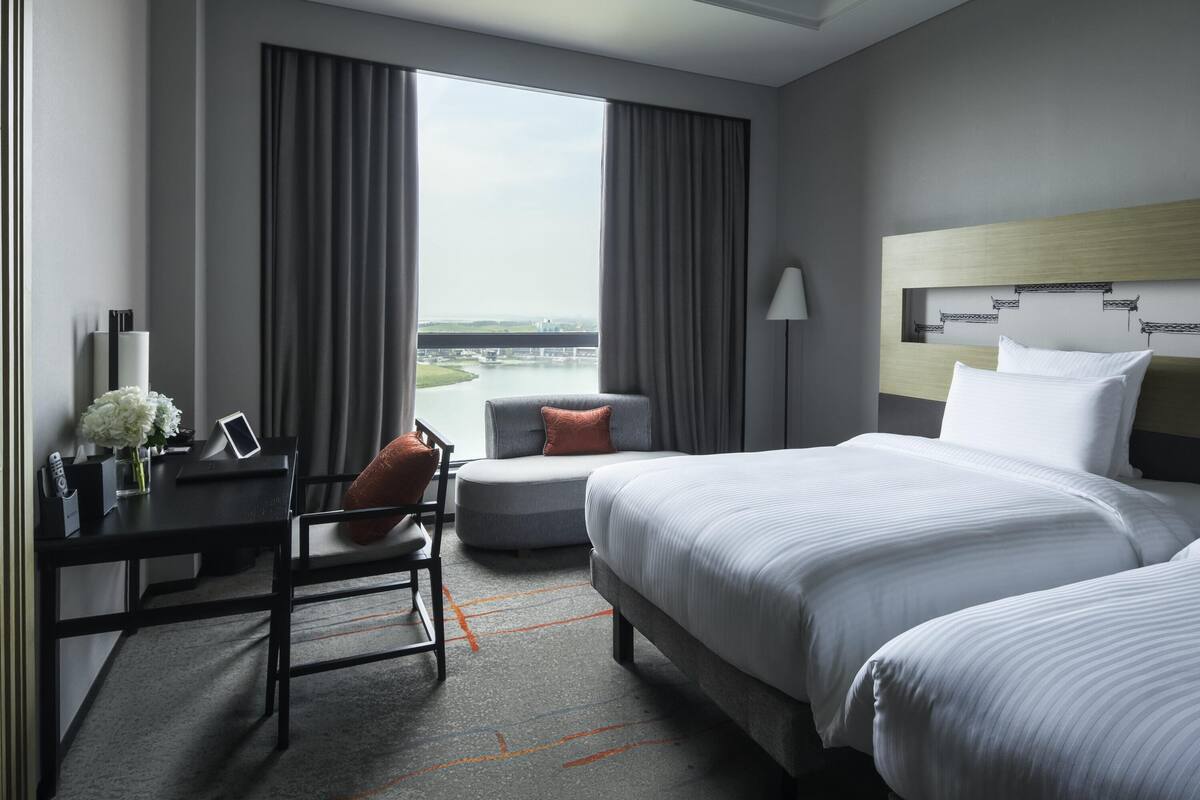 A hotel room with a bed, a desk, a chair, a lamp, and a view of a body of water.