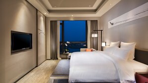 A hotel room with a large bed, a flat-screen TV mounted on the wall, a nightstand with a lamp, and a view of the city at night through the window. - Pullman Hefei Sunac (Hefei)