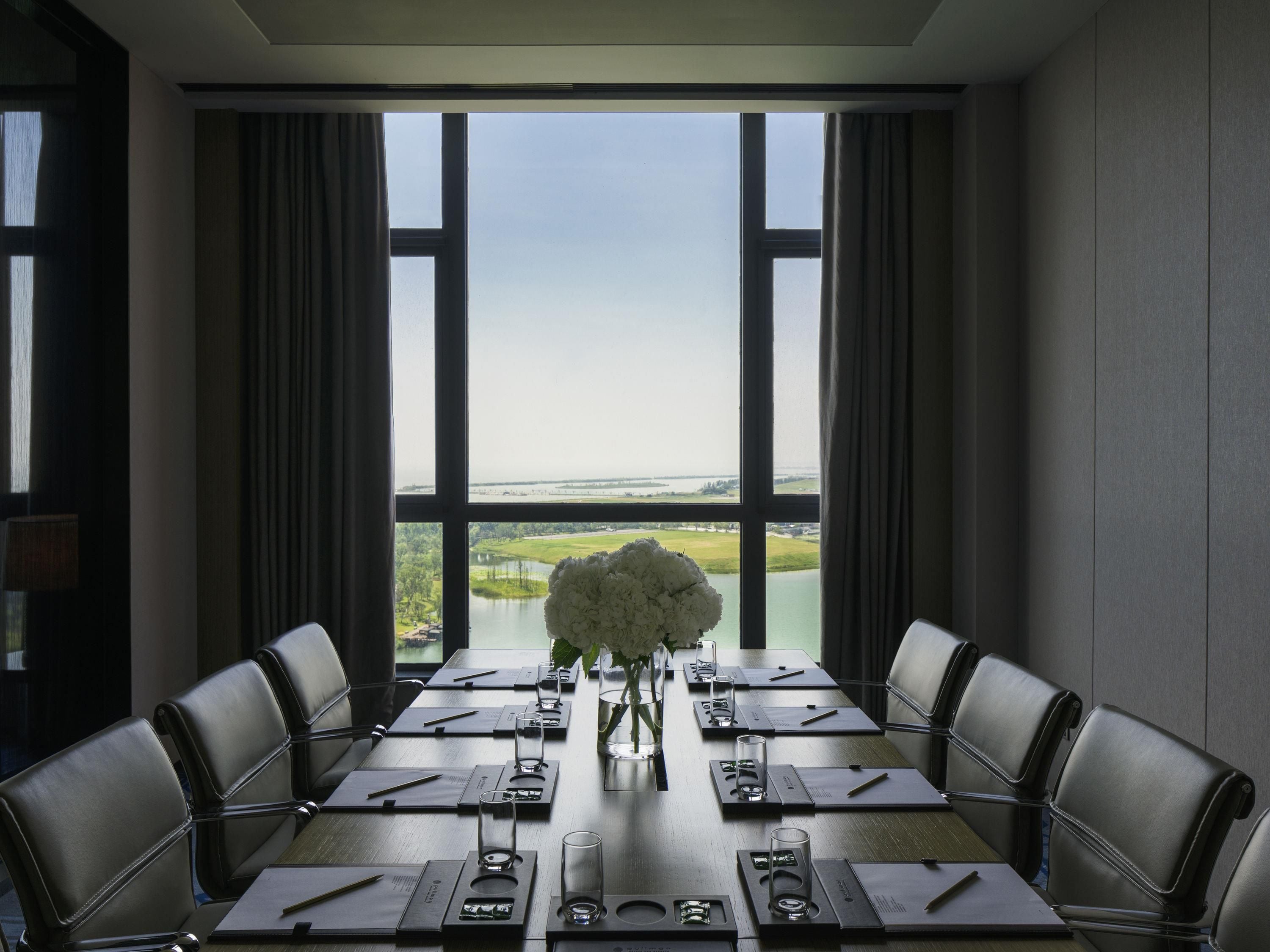 A conference room with a large table, chairs, and a view of a lake through large windows.
