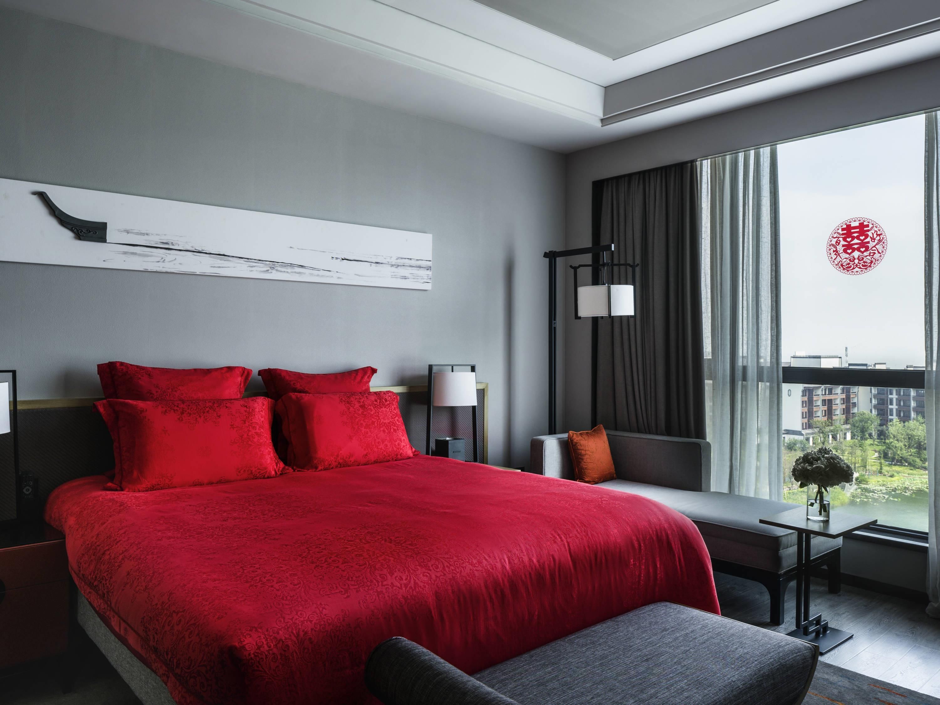 Habitación de hotel moderna con una cama grande, una mesita de noche, un escritorio y vistas de la ciudad a través de amplios ventanales.