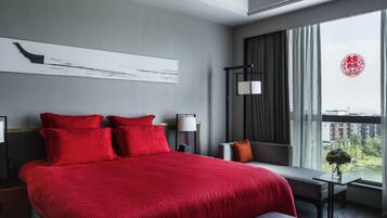 Habitación de hotel moderna con una cama grande, una mesita de noche, un escritorio y vistas de la ciudad a través de amplios ventanales.