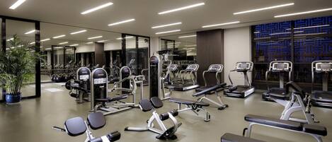 A modern gym with various exercise equipment, large mirrors, and a potted plant.