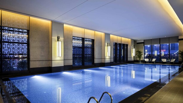 A modern indoor swimming pool with a clear blue water surface, surrounded by walls with geometric patterns and ambient lighting. - Pullman Hefei Sunac (Hefei)