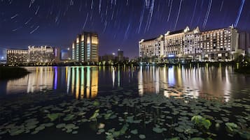 Nachtszene mit Sternspuren über einem Gewässer, das Gebäude widerspiegelt, darunter ein Hotel mit mehreren Etagen und Balkonen.