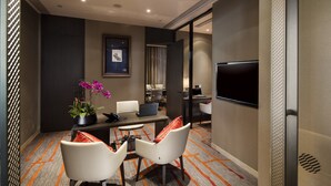 A modern hotel room with a large flat-screen TV, a desk with a laptop, two white chairs, a potted plant, and a framed picture on the wall. - Pullman Hefei Sunac (Hefei)