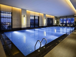 A modern indoor swimming pool with a clear blue water surface, surrounded by walls with geometric patterns and ambient lighting. - Pullman Hefei Sunac (Hefei)