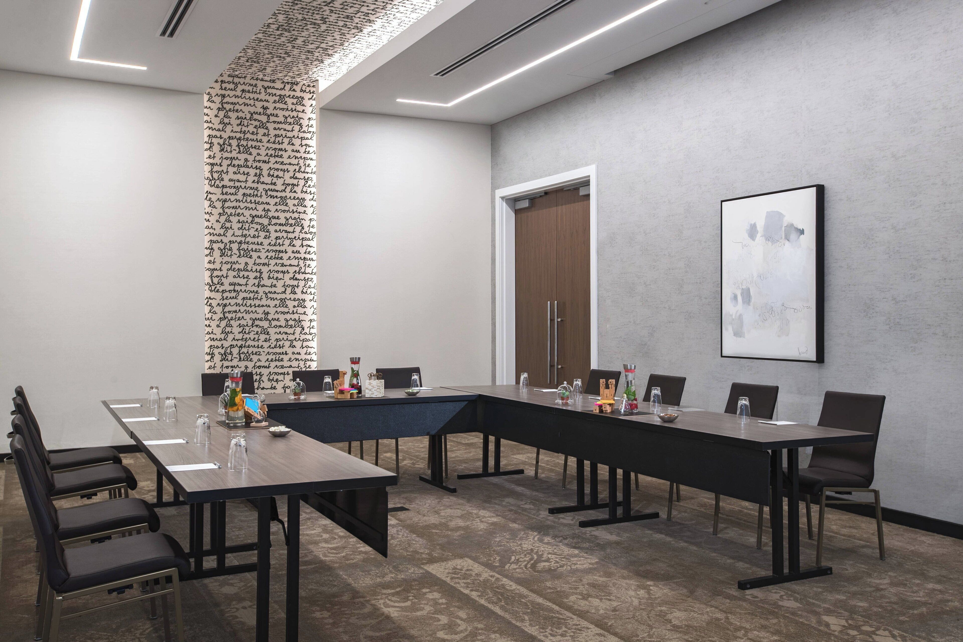 Un salón de conferencias con una larga mesa, sillas y un elemento decorativo en la pared.