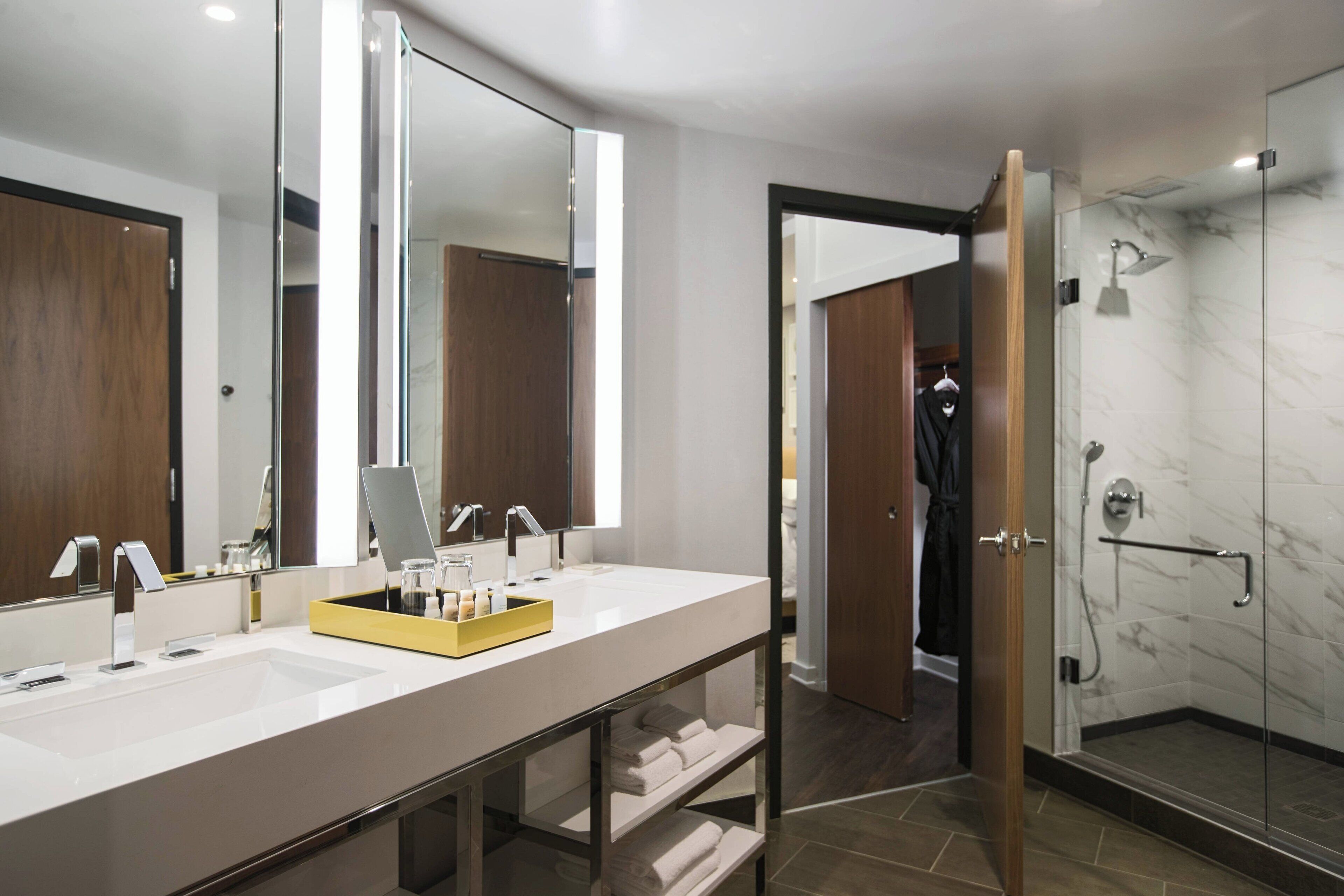 A modern bathroom with a large mirror, two sinks, and a shower area.