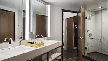 A modern bathroom with a large mirror, two sinks, and a shower area.