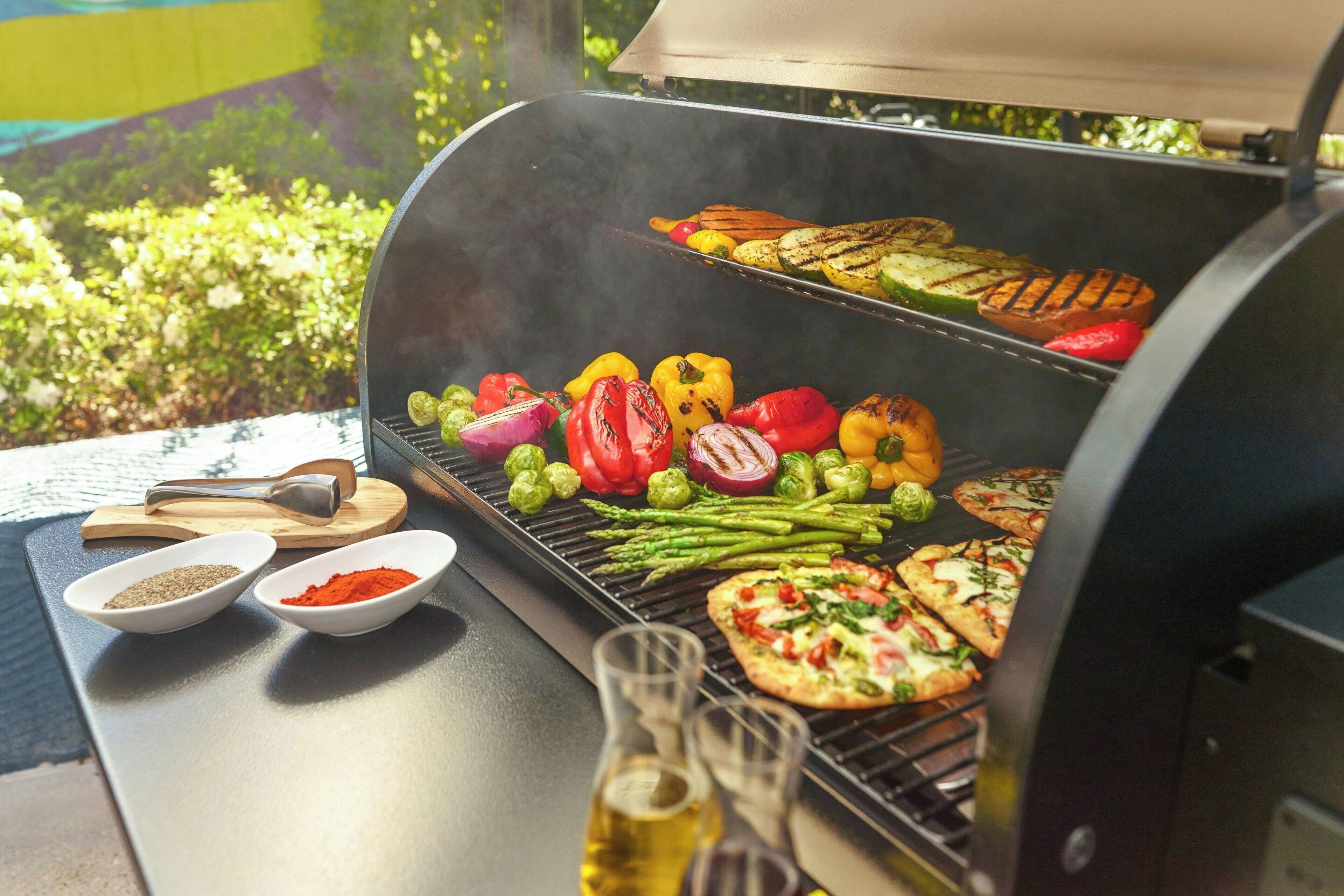 A barbecue grill with vegetables and pizzas being cooked.