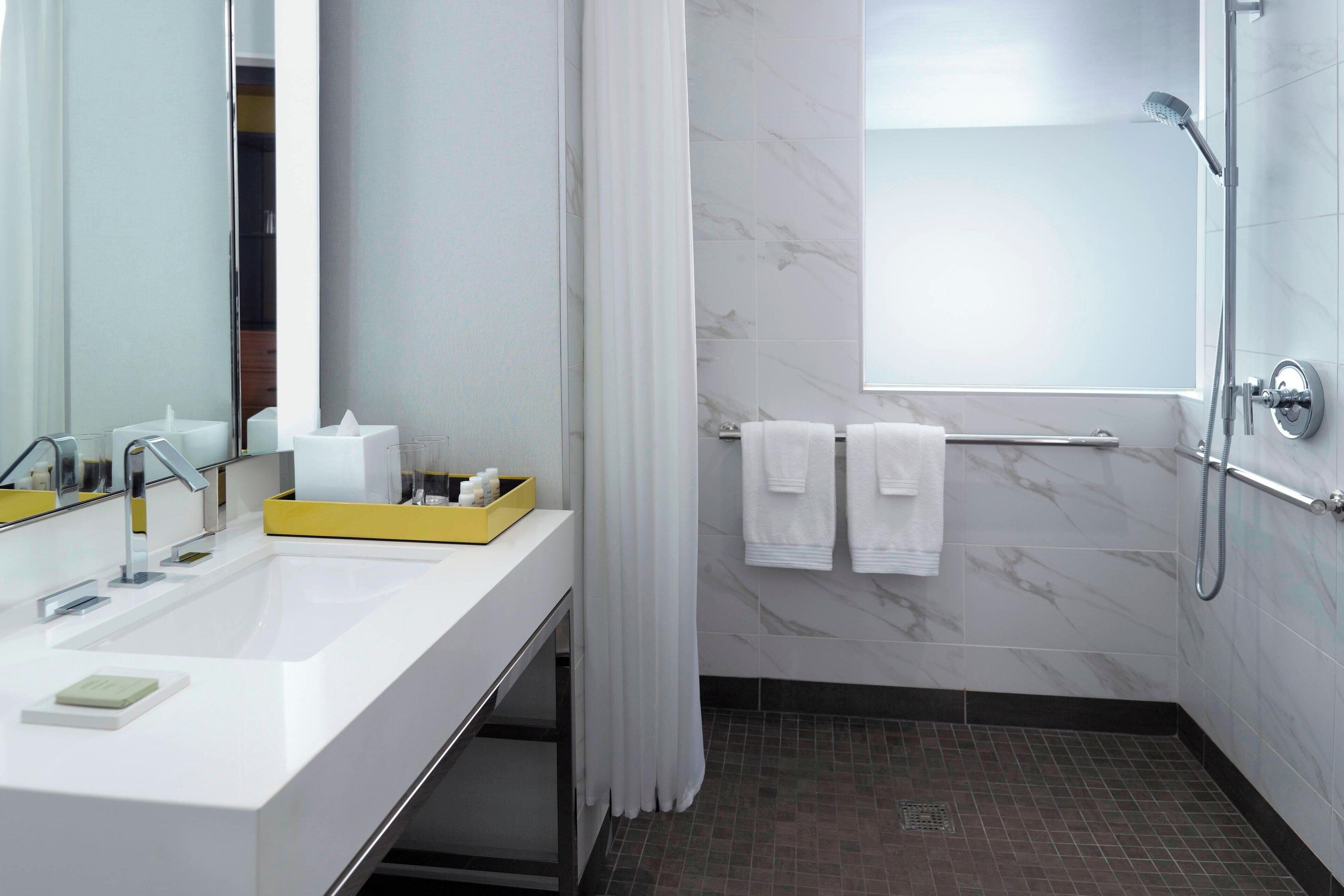 Un baño moderno con un espejo grande, dos lavamanos, una ducha y un perchero para toallas.