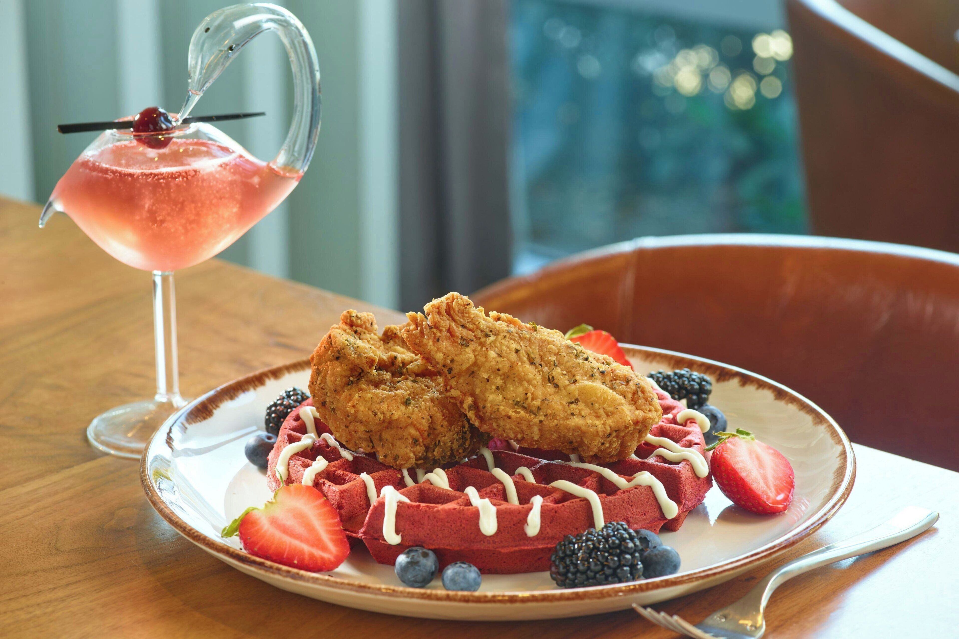 A plate with waffles, strawberries, blueberries, blackberries, and a fried chicken piece.