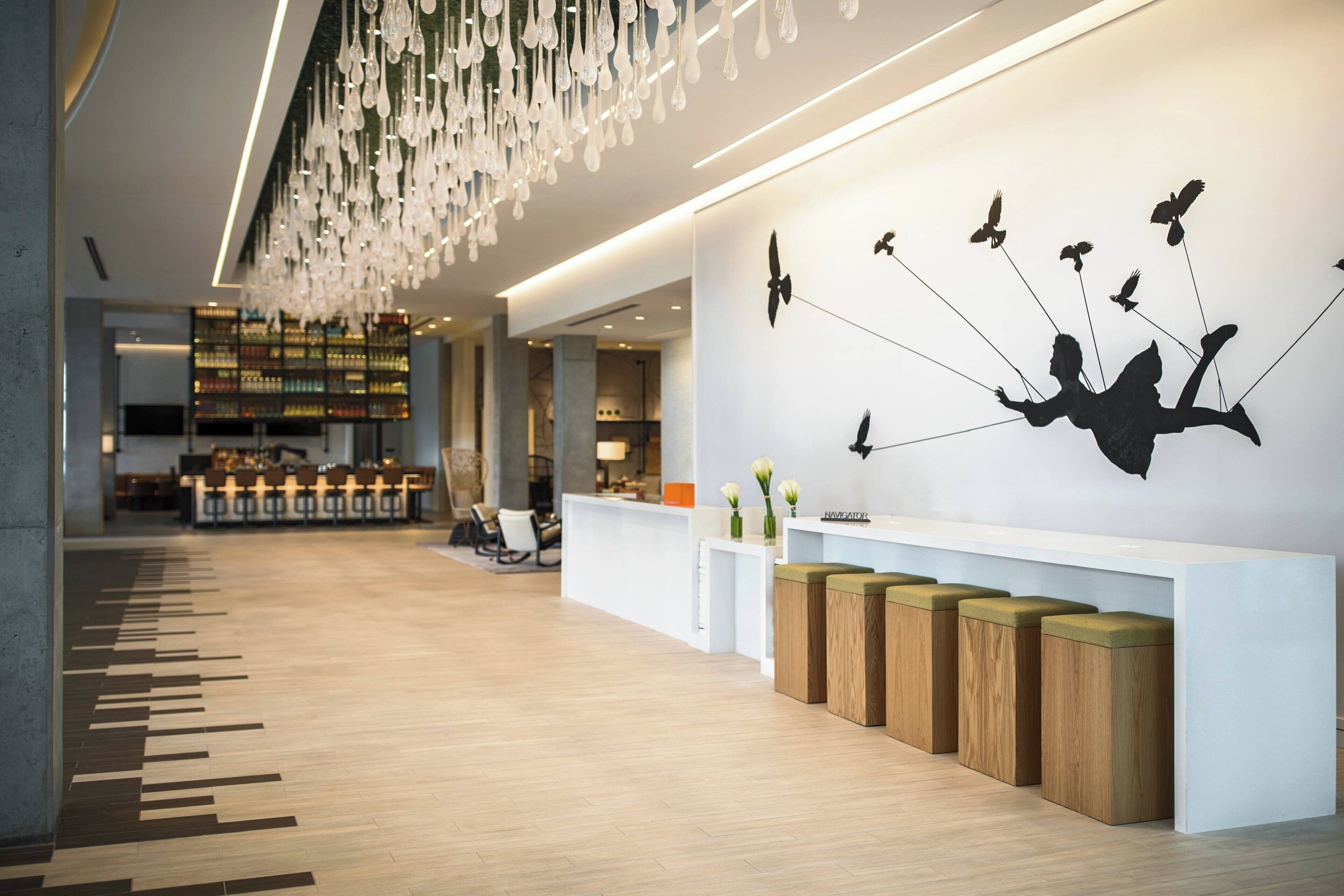 Un espace d’accueil moderne avec un plancher en bois, un comptoir d’accueil blanc et une œuvre d’art murale représentant une personne volant avec des oiseaux.