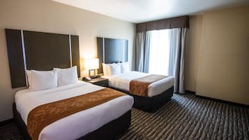 Habitación de hotel con dos camas, una mesita de noche, una lámpara y un ventanal con cortinas.