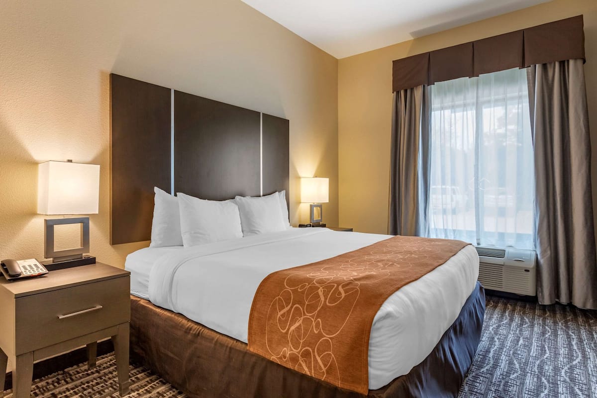 Une chambre d’hôtel avec un grand lit, deux tables de chevet avec des lampes, un téléphone et une fenêtre avec des rideaux.