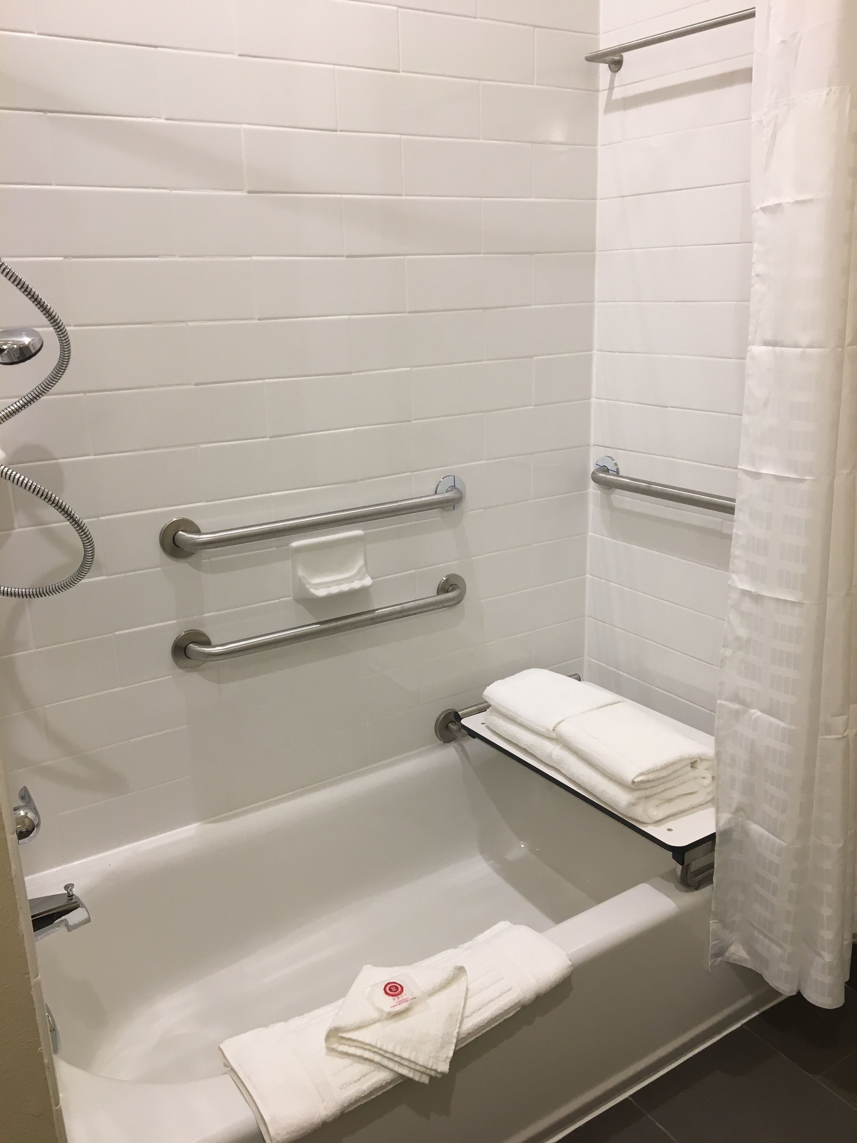 Een moderne badkamer met witte betegelde wanden, een badkuip met een glazen plank en een douchegedeelte met gordijn.