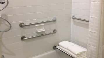 Een moderne badkamer met witte betegelde wanden, een badkuip met een glazen plank en een douchegedeelte met gordijn.