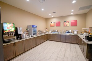 Une cuisine bien éclairée, équipée d’une machine à café, d’un réfrigérateur et de divers produits alimentaires disposés sur le plan de travail.